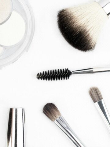 Assorted makeup brushes, a brow spoolie, and a compact with three powders arranged on a white surface-perfect essentials to update your look and feel more beautiful every day.