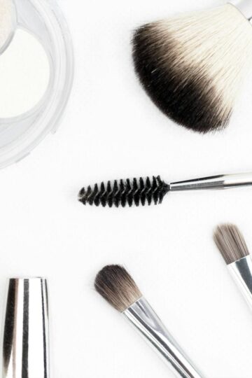 Assorted makeup brushes, a brow spoolie, and a compact with three powders arranged on a white surface—perfect essentials to update your look and feel more beautiful every day.