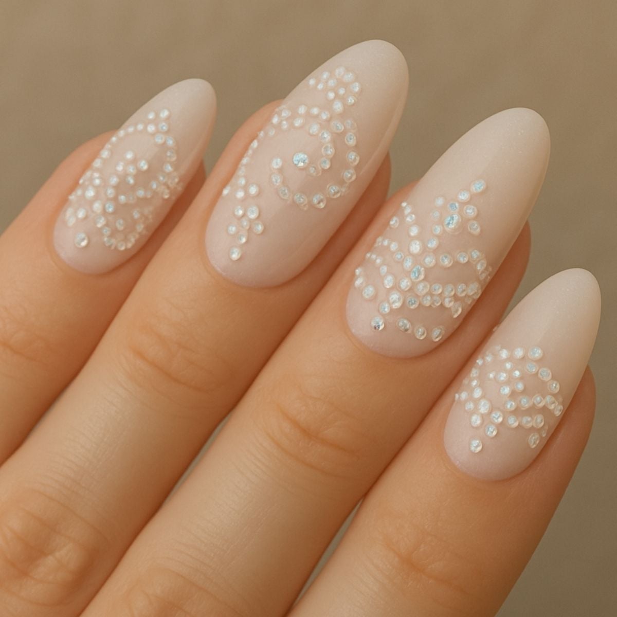 Four manicured fingernails with a matte nude base, each decorated with intricate white swirl patterns featuring sparkling crystals—perfect for fans of elegant Crystal Nail Art.