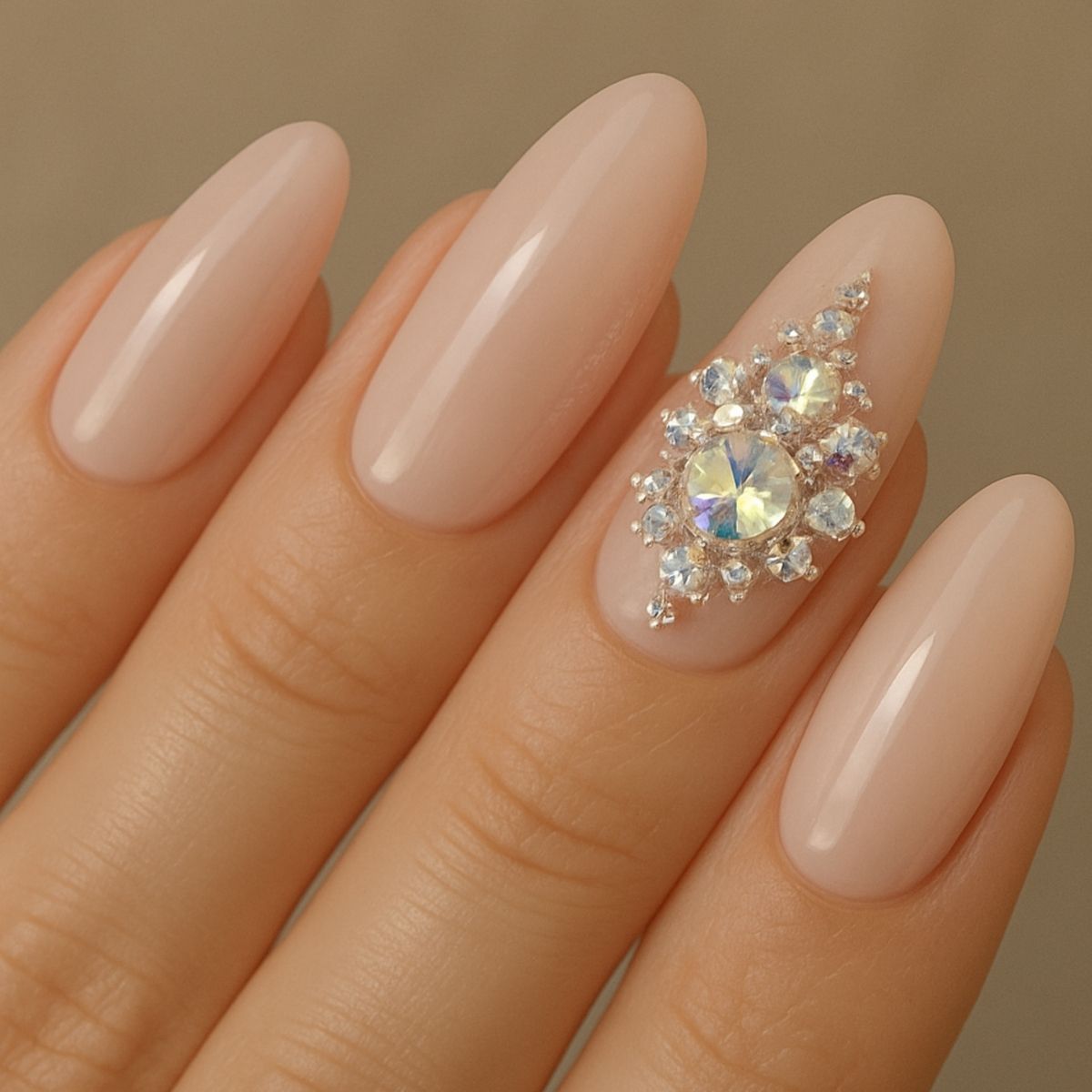 A hand with long, almond-shaped nude nails; the ring finger features dazzling Swarovski Nail Designs and gem decorations.
