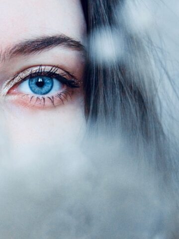 Close-up of a person's blue eye and eyebrow, with part of their face obscured by a soft, out-of-focus foreground.