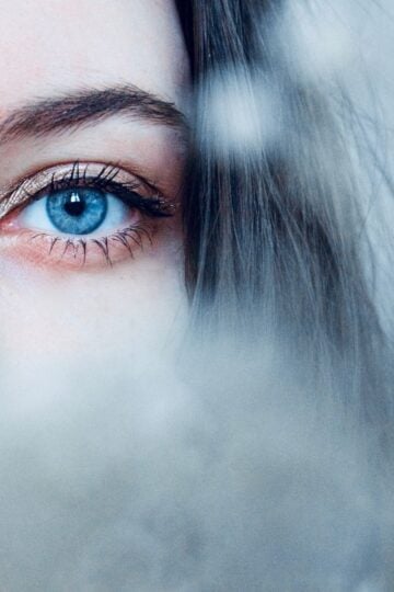 Close-up of a person's blue eye and eyebrow, with part of their face obscured by a soft, out-of-focus foreground.