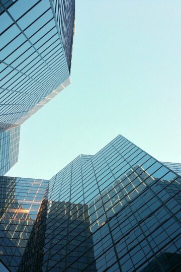 Tall modern glass office buildings with reflective windows rise against a clear blue sky, viewed from a low-angle perspective—an ideal setting for innovative business management consulting by Ascot International.