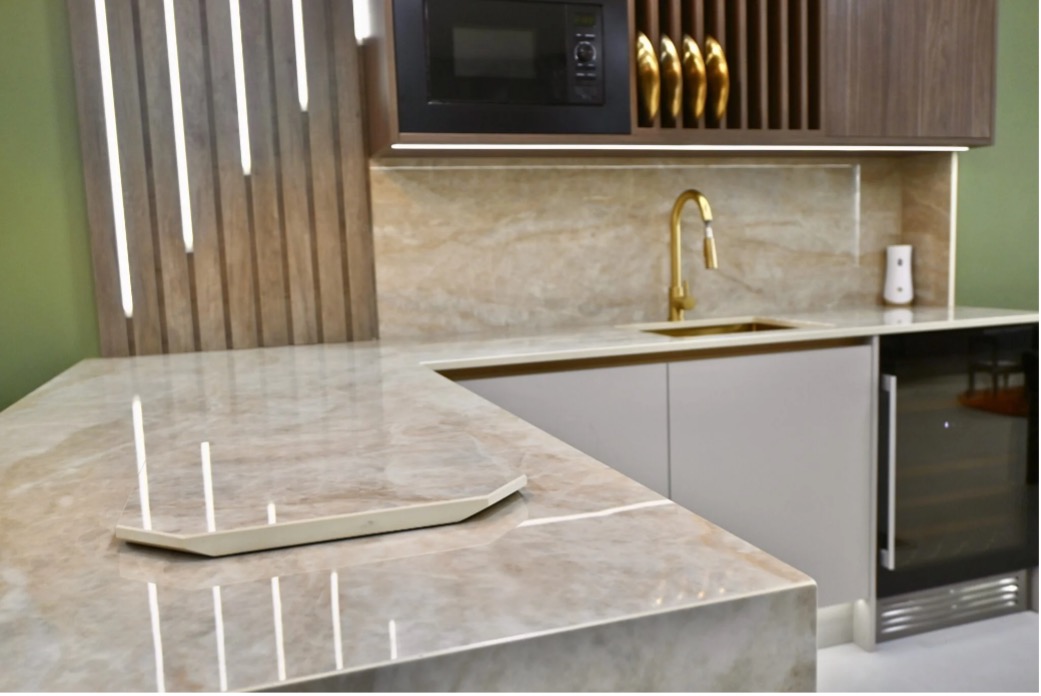 Modern kitchen with quartz countertops, gold faucet, built-in microwave, glass-front fridge, and vertical wood slats on a green accent wall.