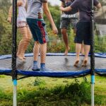 Four children are jumping together on an outdoor trampoline in a grassy yard, making it one of the best kids activities and active day out ideas that's fun for parents too.
