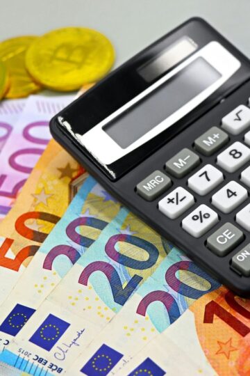 A black calculator rests on euro banknotes and gold-colored coins, symbolizing financial control and the tools needed to manage finances effectively.