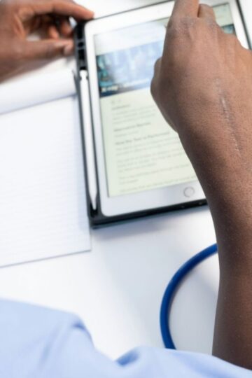 A person uses a tablet with a notepad and stethoscope on the desk, suggesting a medical or healthcare setting.