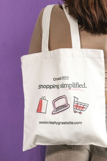 A person with long brown hair carries a white tote bag that says "shopping simplified," featuring icons of a bag, laptop, and shopping cart on a purple background—perfect for those who love custom designs and tote bag printing.