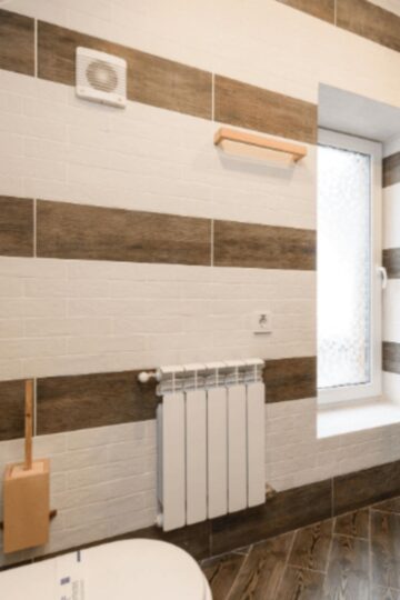 Modern bathroom with horizontal brown and white tile stripes, stylish radiators to warm your home, frosted window, wooden shelves, and part of a toilet visible in the foreground.