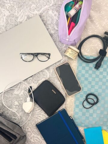 A collection of University Essentials-including a laptop, eyeglasses, charger, and more-are neatly arranged on a patterned surface. Find all these Clever Buys to stay organized and ready for campus life.