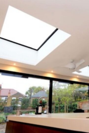 Modern kitchen interior with stylish roof lights in the ceiling and a wide glass wall revealing a view of houses and greenery—a perfect blend of home design and natural beauty.