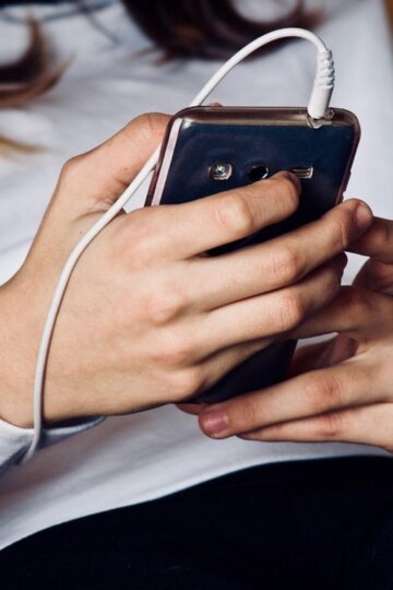 A person wearing a white long-sleeve shirt holds a smartphone with a white cord plugged into it, emphasizing the importance of smartphone security.