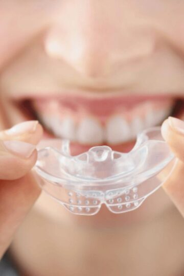 A person holds a clear dental mouthguard close to their mouth, about to place it over their upper teeth—one of the latest Night Guards for 2025 designed to promote restful sleep.