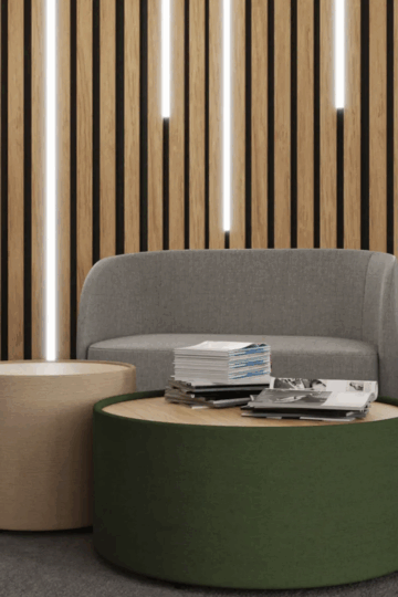 A modern lounge area with gray sofas, quality round green and beige coffee tables, stacked magazines, and a wooden slat wall with vertical lighting strips offers comfort and style—ideal for mental health furniture environments.