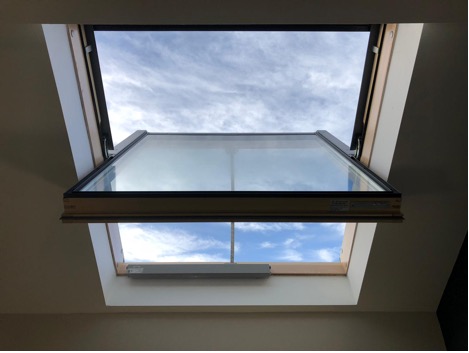 A skylight window partially open, showing a view of blue sky with scattered clouds.