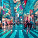 People walk across a brightly lit street in a busy city area at night, surrounded by tall buildings and colorful neon signs-an exciting scene for those who want to explore Tokyo and enjoy stress-free travel.