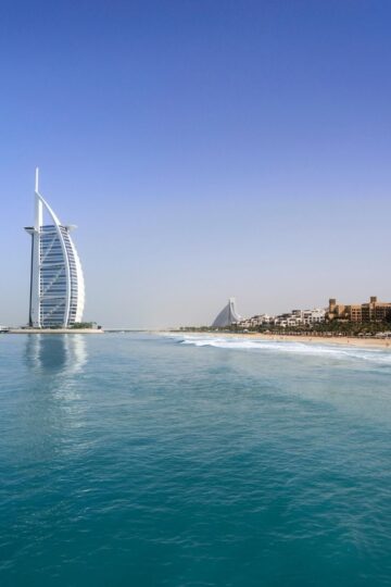A view of the Burj Al Arab hotel on the coastline with golden sand, blue sea, and a clear sky in Dubai, set against stunning skylines.