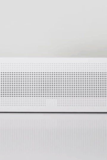A white rectangular wireless speaker with a perforated front panel sits on a glossy surface, resembling the sleek design of some AC repair tools, against a plain white background.