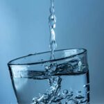 A stream of premium water is being poured into a clear glass, causing bubbles and ripples, against a blue background-crafted for true connoisseurs.