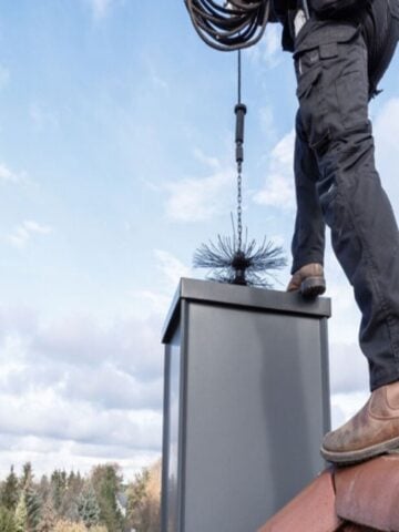 A person standing on a rooftop prepares to clean a chimney using a chimney brush attached to a rod, helping improve indoor air quality-essential for homes in need of professional Chimney Cleaning Fort Worth services.