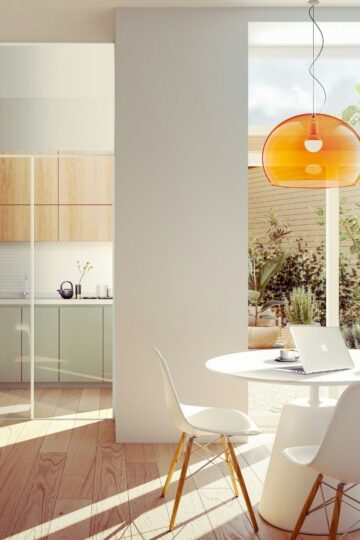 A modern kitchen and dining area with wooden floors, white chairs, a round table, potted plants, and large windows—designed to maximize space and let natural light fill your home.