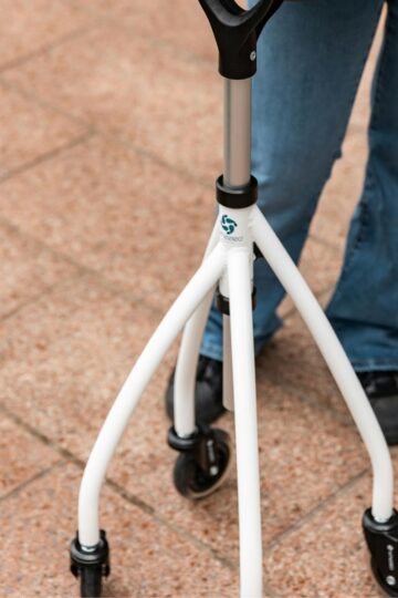 Person wearing blue jeans and black shoes stands on a tiled surface, confidently using a white mobility aid with three wheels, highlighting how mobility aids can support independence and mental well-being.