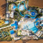 Aerial view of a large waterpark featuring pools, winding water slides, lazy rivers, lounge chairs, and surrounding fields-perfect for a fun-filled family resort getaway.