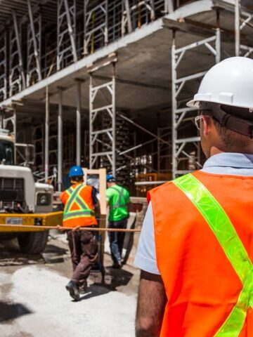 Construction workers in safety gear and hard hats are working near a large truck at a residential construction site, with scaffolding in the background showcasing effective project management.