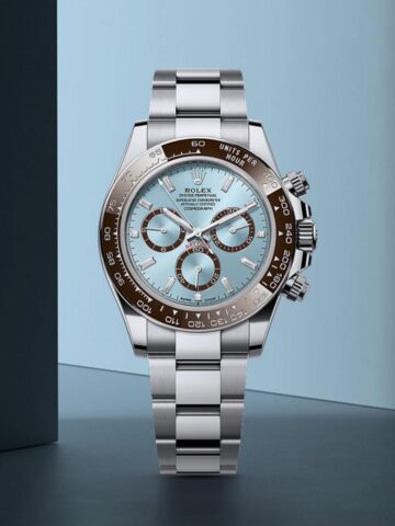 A Rolex wristwatch with a silver metal band, brown bezel, and light blue face with three subdials, displayed upright against a blue background.