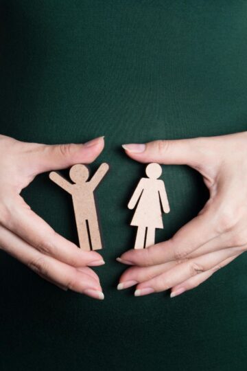 Person in a green dress holds two wooden cutouts of a boy and a girl with both hands in front of their abdomen, symbolizing how education for change can make a difference in young lives.