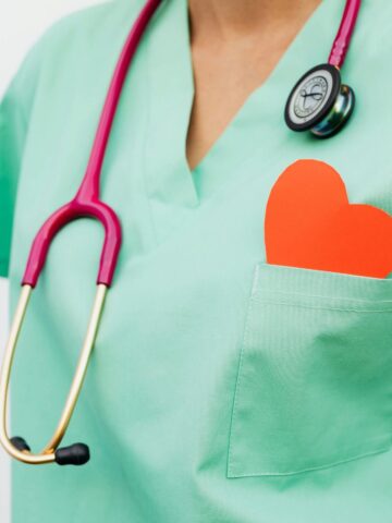 A person wearing green medical scrubs with a stethoscope around their neck and a red paper heart in their chest pocket, symbolizing the core qualities of exceptional nurses.