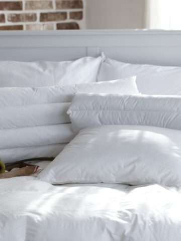A neatly made bed with white cotton percale bedding and pillows, a wooden tray holding a green apple, mug, and book-perfect for busy homes-set in a bright room with a white headboard and brick accent wall.
