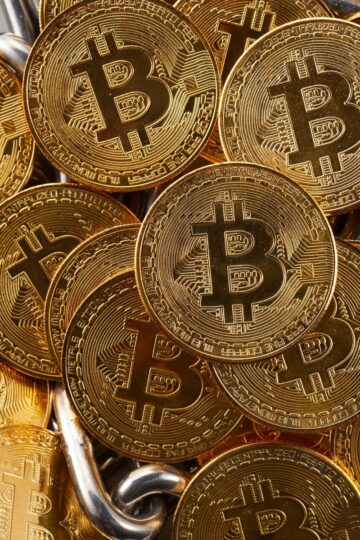 A pile of shiny gold-colored coins with the Bitcoin symbol embossed on them, arranged closely together.
