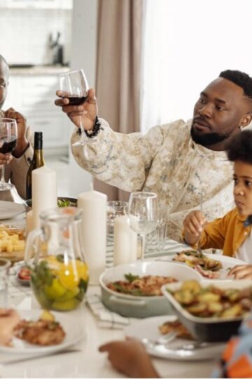 A family sits around a dining table sharing a meal; two adults raise wine glasses for a toast while children eat, highlighting positive family dynamics.