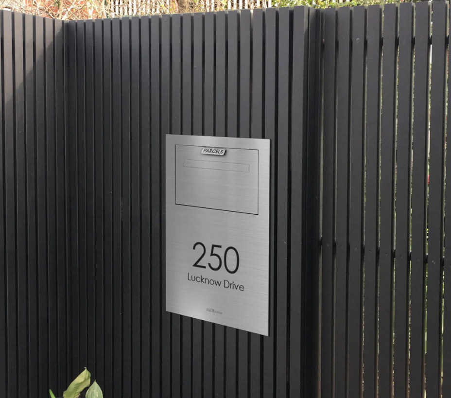 A silver sign on a black slatted fence displays the address "250 Lucknow Drive" with a blank nameplate above it, highlighting the benefits of modern letterboxes for both style and practicality.