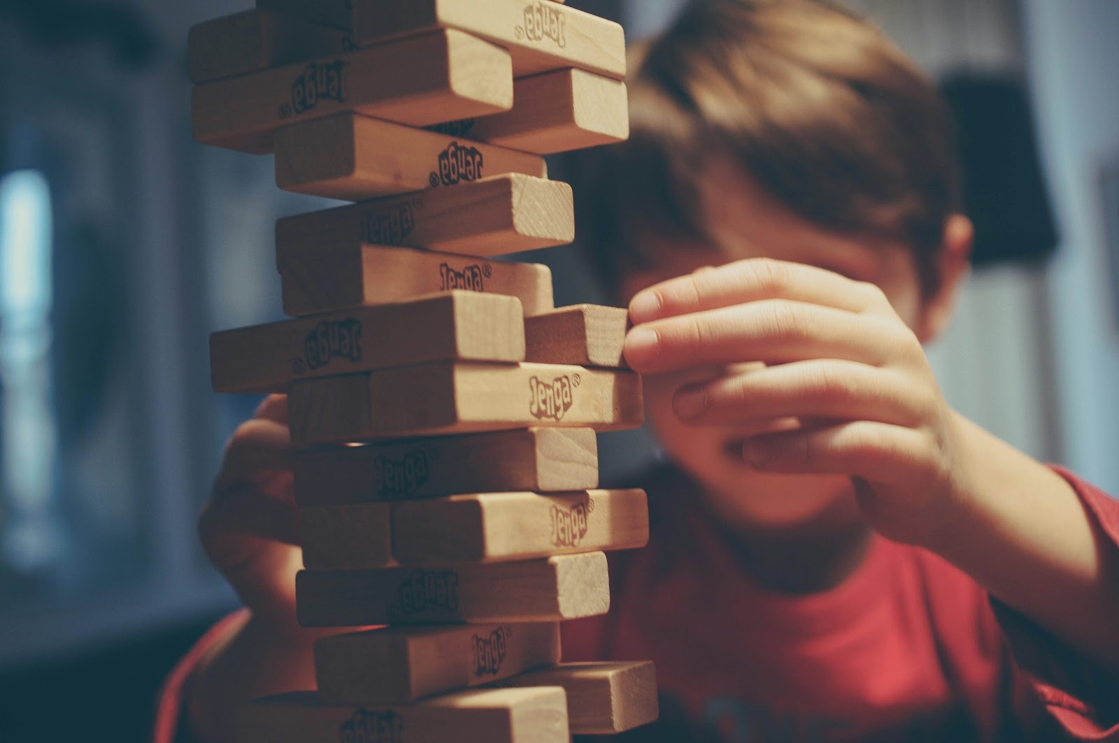A child carefully pulls a wooden block from a stacked Jenga tower, with both hands visible and focused attention on the game.