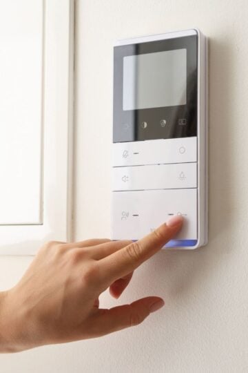 A person presses a button on a wall-mounted control panel with a display screen and several buttons—making energy-efficient upgrades to help lower heating bills.