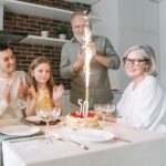 Four people celebrate a 50th birthday at a dining table with a cake, sparkler candle, and number 50 candle in a home kitchen setting-perfect inspiration for milestone celebration ideas.