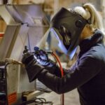 A person wearing a welding helmet and gloves is welding metal pieces together in a workshop, showcasing skills often seen with the best welding brands used in home welding projects.