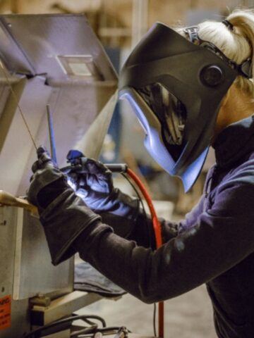 A person wearing a welding helmet and gloves is welding metal pieces together in a workshop, showcasing skills often seen with the best welding brands used in home welding projects.