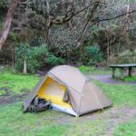 A small dome tent with a backpack and sleeping pad set up on grass in a wooded campsite near a picnic table-perfect for those looking to camp Australia-style. Check out camping tips for an even better outdoor adventure!.