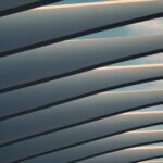 Curved metal beams create a repeating pattern against a partly cloudy sky, showcasing modern metal building style.