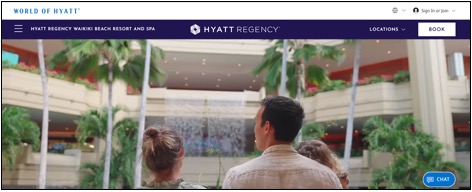 Three people stand indoors facing a large waterfall feature surrounded by palm trees at the Hyatt Regency Waikiki Beach Resort and Spa.