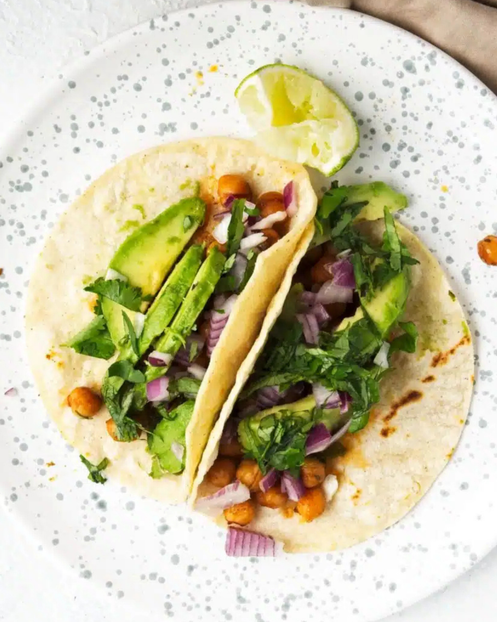 Celebrate With These Recipes for Lunch Ideas on Mother's Day Two soft tacos filled with chickpeas, avocado slices, chopped red onion, and coriander on a white speckled plate with a lime wedge-perfect for easy lunch ideas or festive Mother's Day lunch recipes.