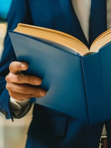 A person in a blue suit holding and reading an open Social Security Blue Book, with a blurred indoor background.