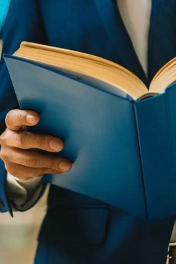 A person in a blue suit holding and reading an open Social Security Blue Book, with a blurred indoor background.
