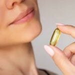 A person holding a large yellow capsule pill near their mouth with their lips slightly parted, highlighting collagen for everyday use and its beauty benefits.