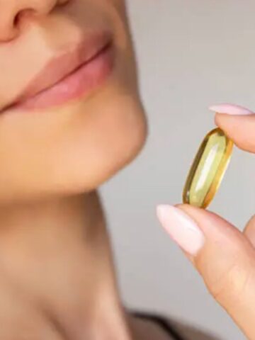A person holding a large yellow capsule pill near their mouth with their lips slightly parted, highlighting collagen for everyday use and its beauty benefits.
