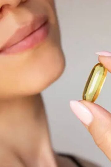 A person holding a large yellow capsule pill near their mouth with their lips slightly parted, highlighting collagen for everyday use and its beauty benefits.
