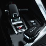 A car key fob rests on a shiny black surface near a modern automatic gear lever-ready for car transport or long-distance removals within the sleek vehicle interior.